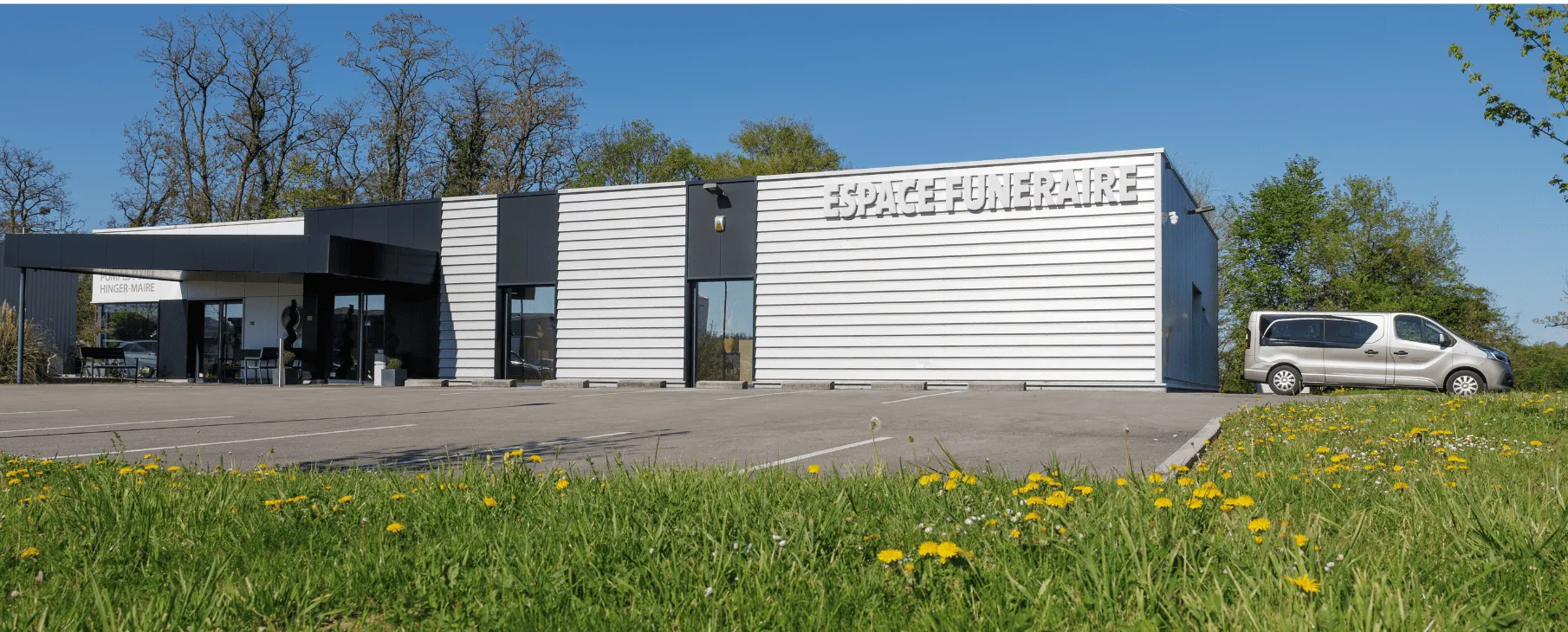 Façade d'une chambre funéraire moderne avec parking et espace vert.